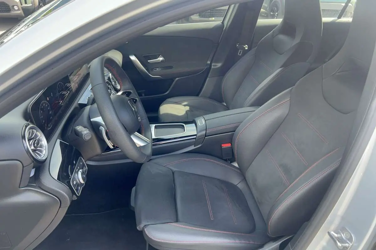 Vue intérieure côté conducteur de la Mercedes Classe A 200 AMG Line 2025 avec sièges sport noirs et surpiqûres rouges.