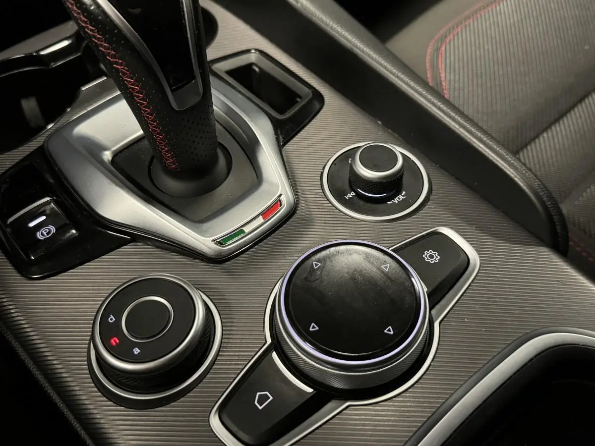 Gros plan sur la console centrale grise de l'Alfa Romeo Giulia 2.2 D 190 BVA Super avec sélecteur de mode et molette de contrôle.