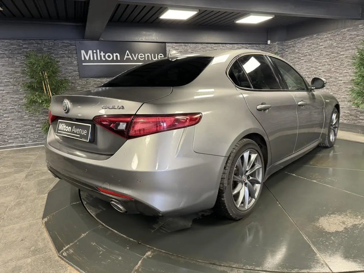 Vue 3/4 arrière droite d'une Alfa Romeo Giulia gris métallisé avec jantes alliage 18 pouces Aero Scuro dans un showroom.