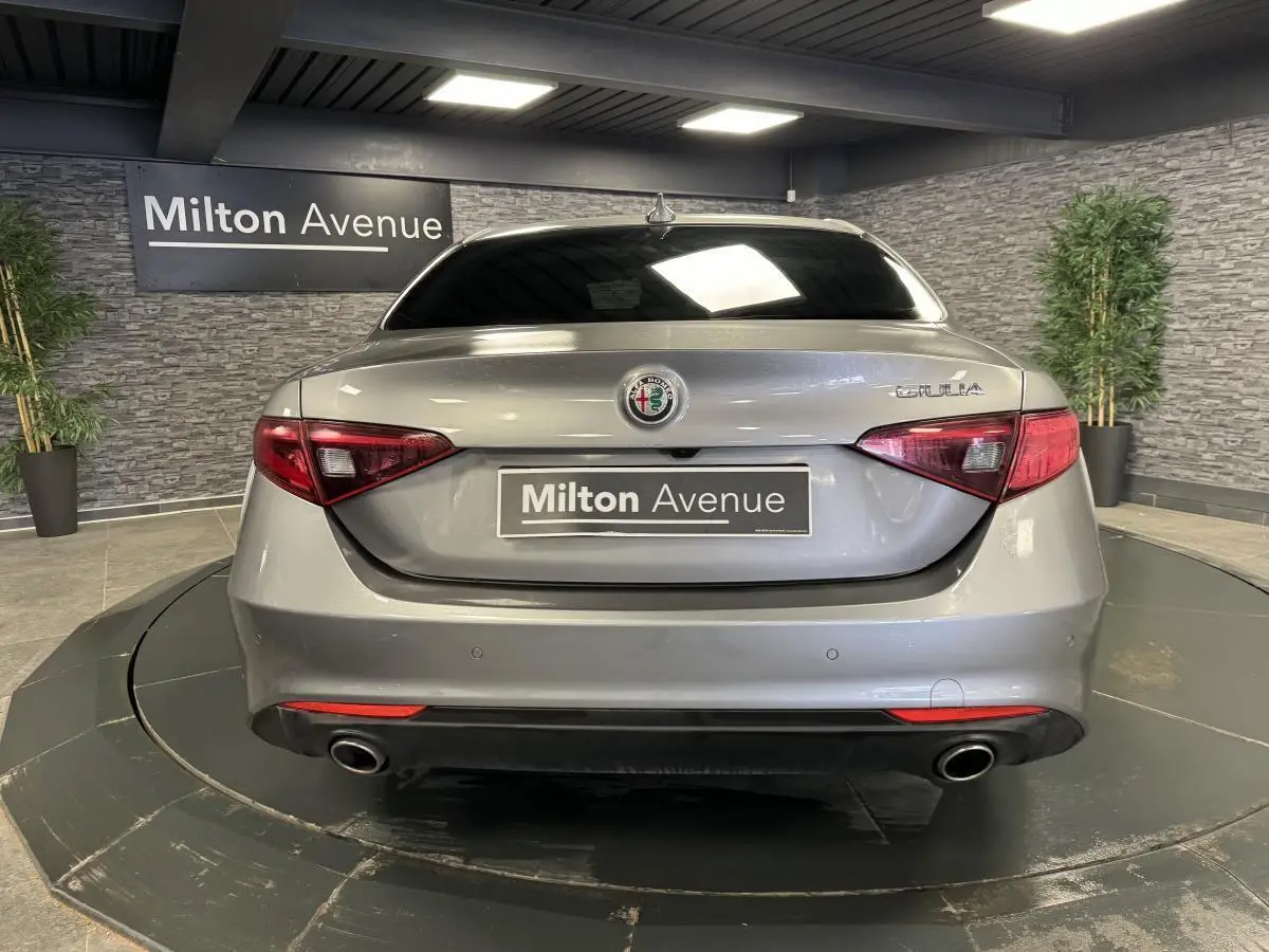 Vue arrière d'une Alfa Romeo Giulia gris métallisé avec feux LED et double sortie d'échappement dans un showroom.
