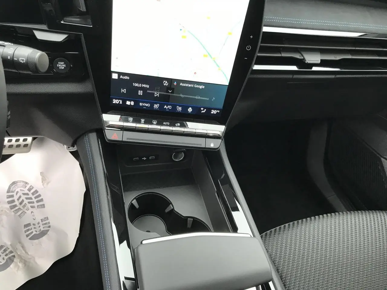 Vue intérieure centrée sur la console centrale noire brillante avec écran tactile vertical et sièges tissu gris.