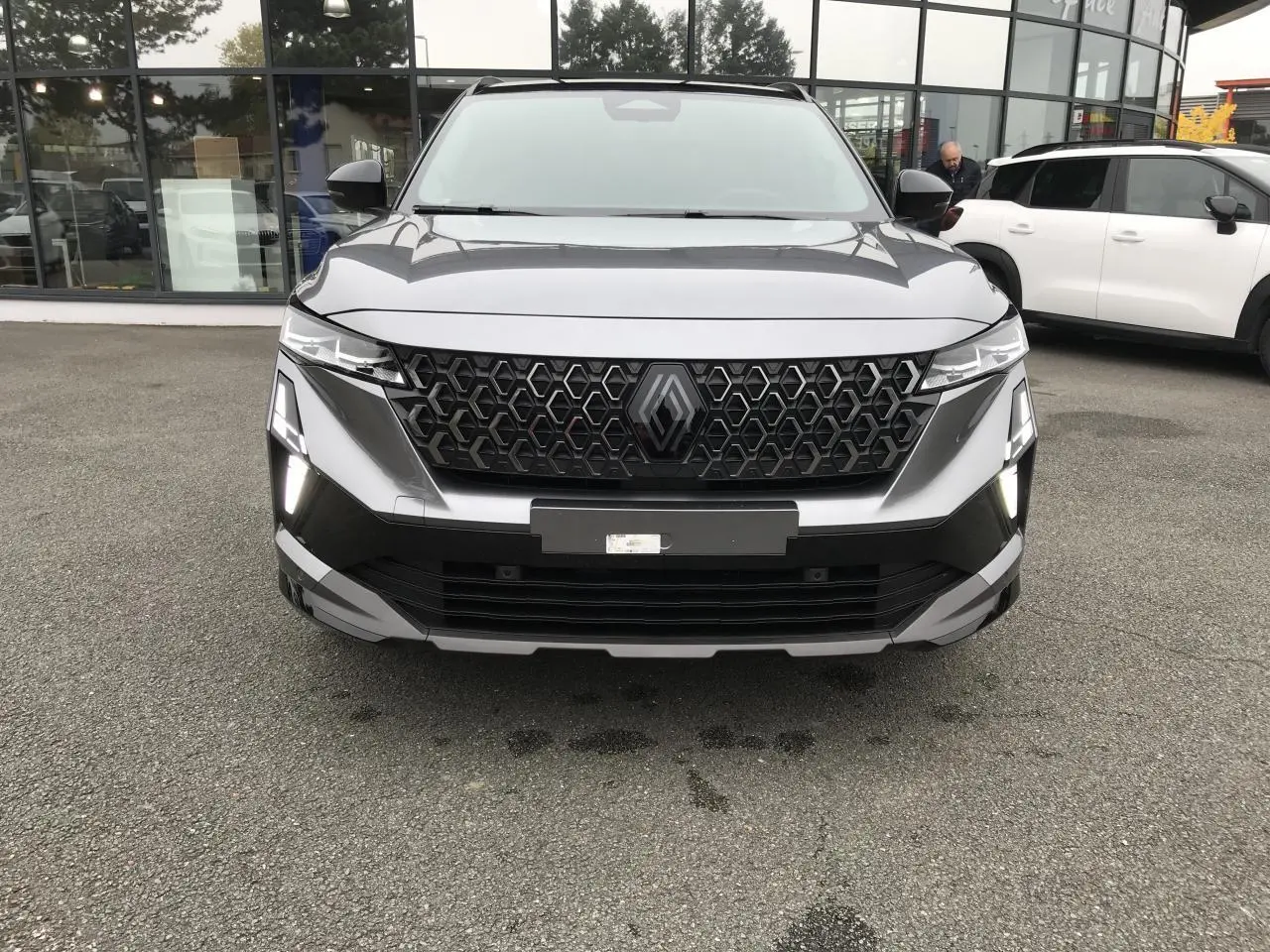 Vue frontale du Renault Austral gris métallisé avec calandre noire à motif hexagonal et feux LED allumés.