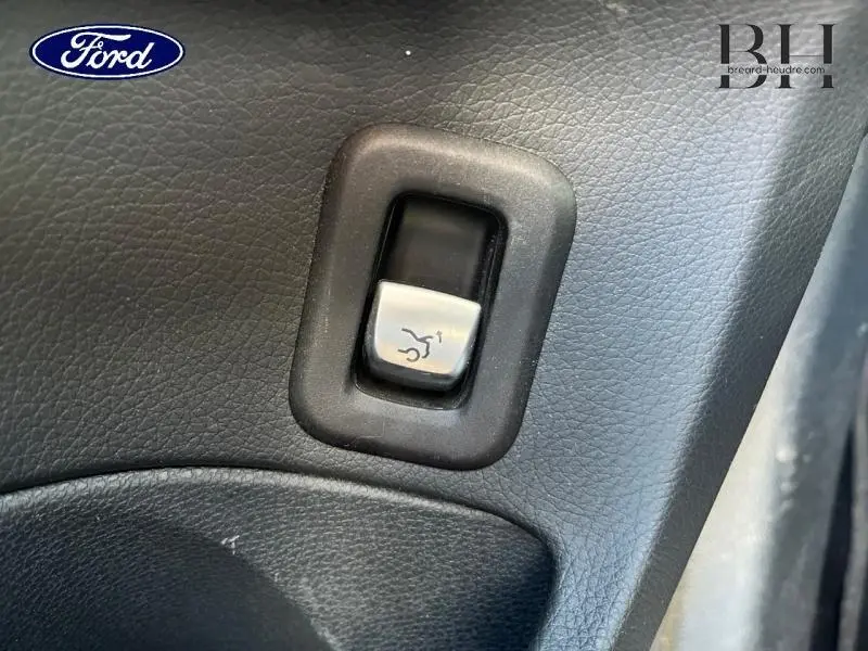 Bouton de déverrouillage du coffre en gros plan sur panneau intérieur noir d'un véhicule.