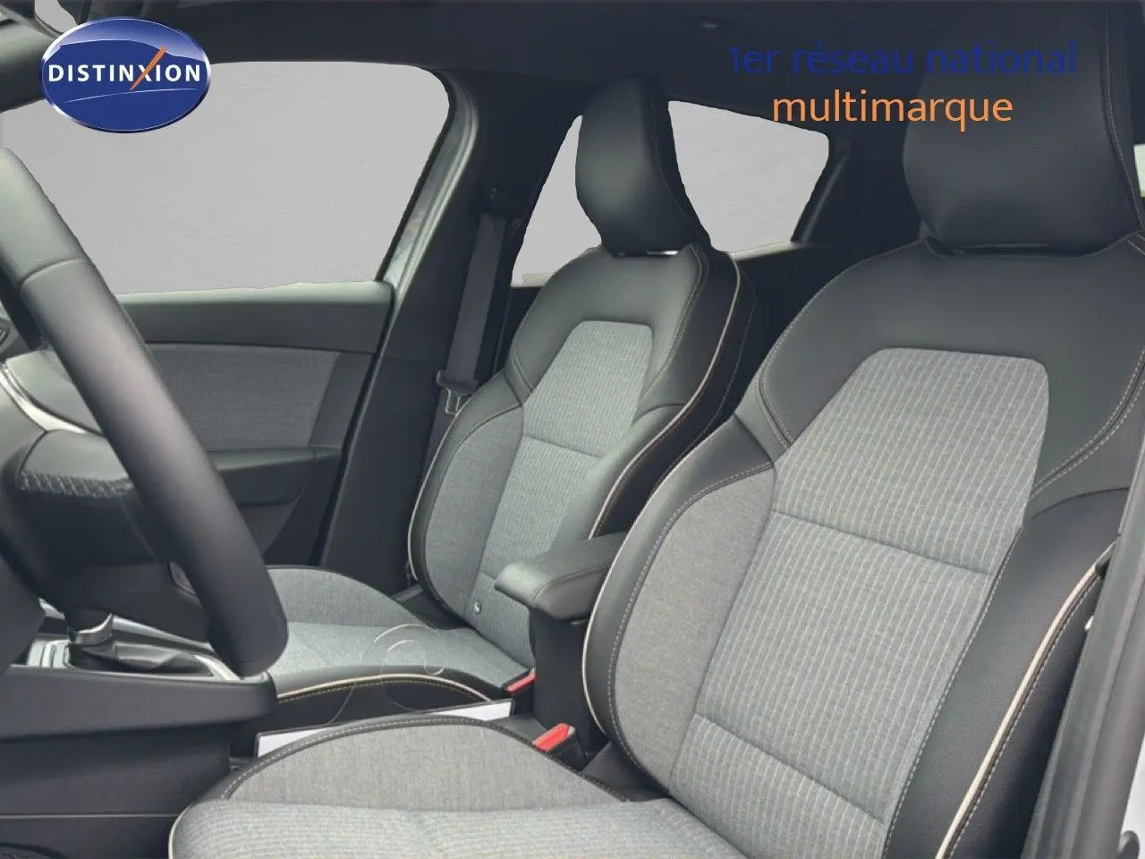 Vue intérieure côté conducteur de la Renault Clio 2025, sièges gris clair avec surpiqûres contrastantes et volant cuir multifonction.