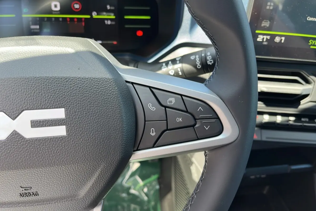 Gros plan sur le volant cuir à commandes multifonctions du DACIA Bigster 2025, avec tableau de bord numérique en arrière-plan.