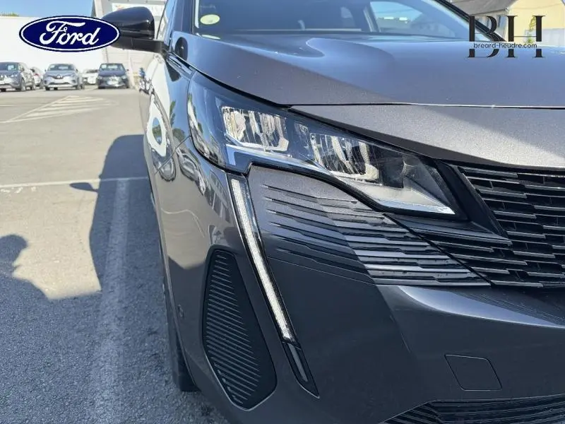 Gros plan sur l'avant droit du Peugeot 5008 gris Platinium, mettant en valeur son phare LED et la calandre noire.