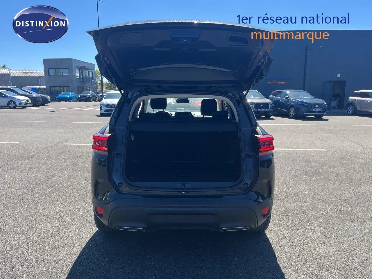 Vue arrière d'un Citroën C5 Aircross noir métal 2025 avec coffre ouvert sur parking extérieur ensoleillé.