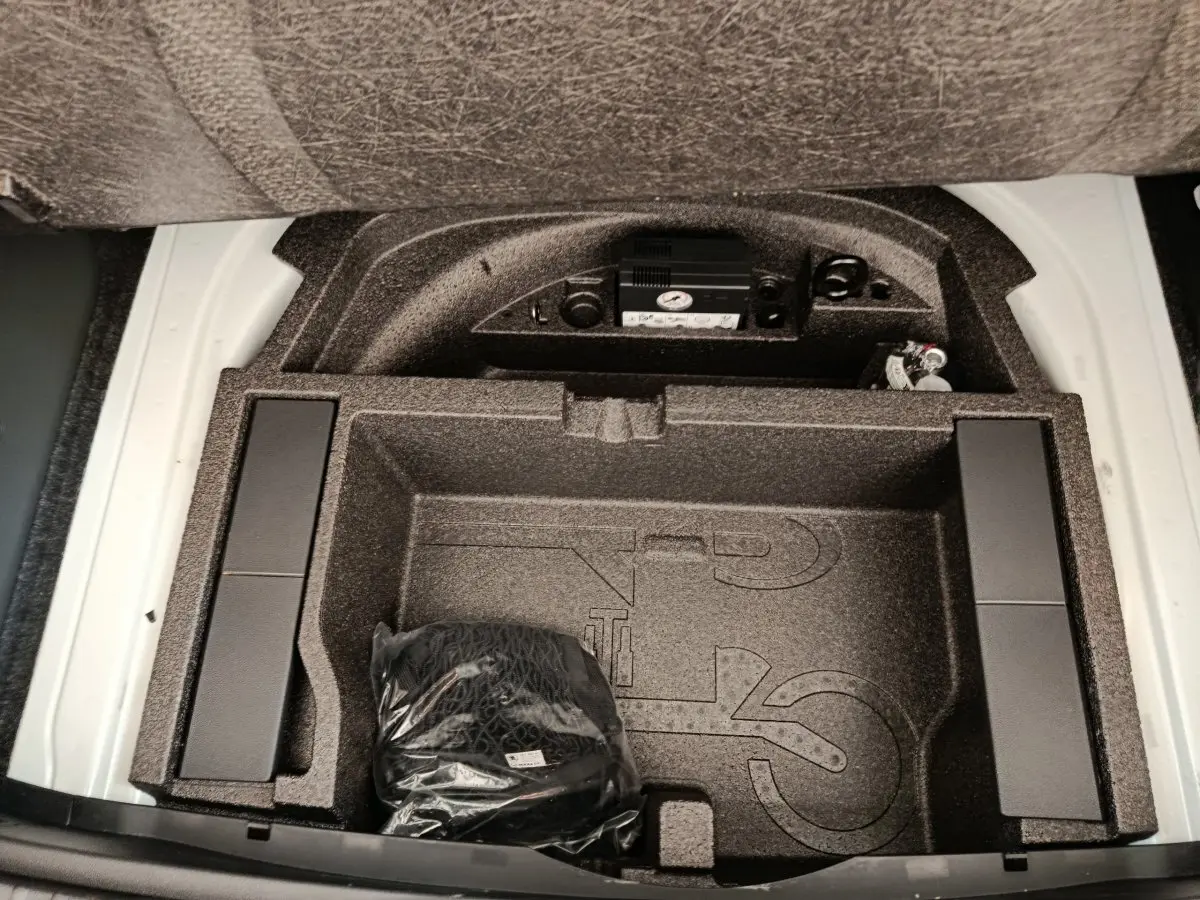 Coffre ouvert d’une Skoda Octavia blanche, vue de dessus sur le rangement sous plancher avec accessoires intégrés.