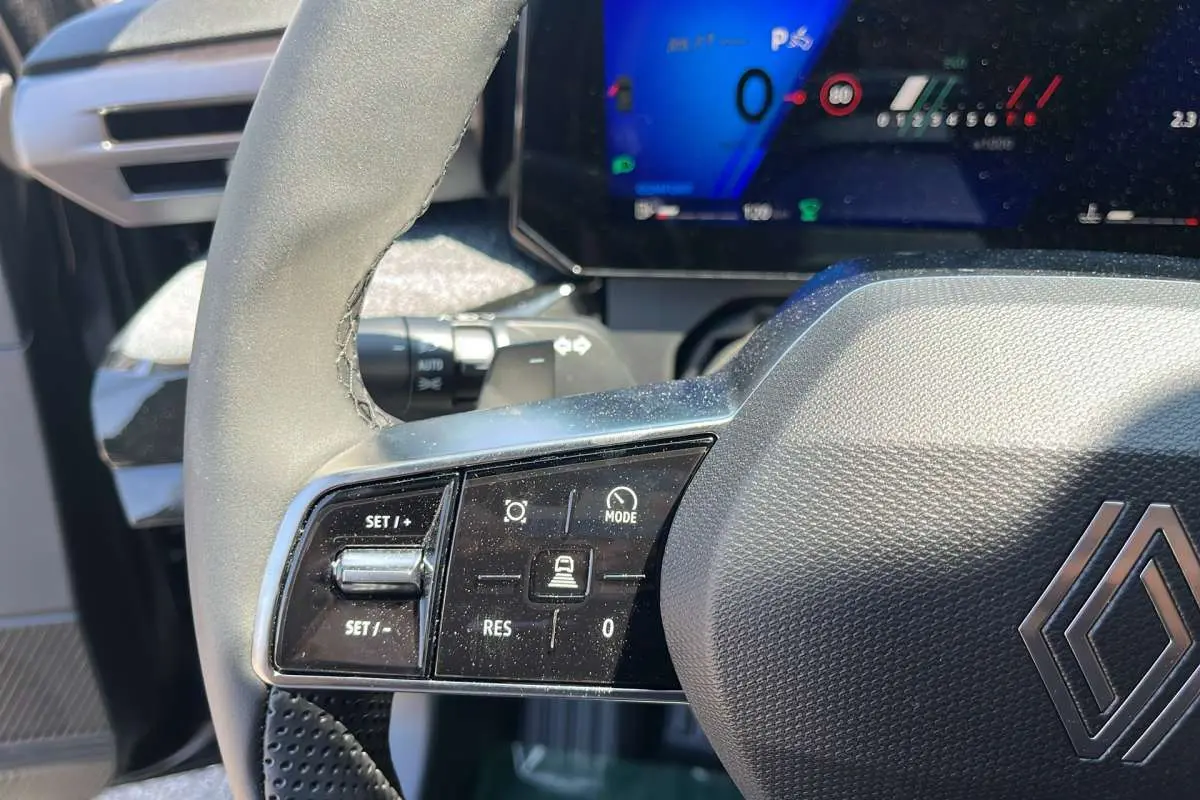 Gros plan sur le volant noir texturé de la Renault Clio 6 TCE 115 EDC TECHNO PLUS avec commandes multifonctions et tableau de bord digital.
