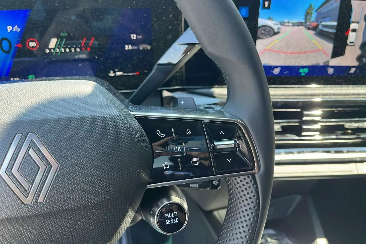 Gros plan sur le volant textile grainé noir étoilé de la Renault Clio 6 TCE 115 EDC avec commandes multifonctions et écran tactile.