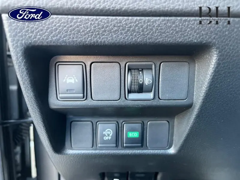 Panneau de commandes noir avec boutons d'aide à la conduite et régulation d'éclairage, intérieur d'un Nissan Qashqai gris.