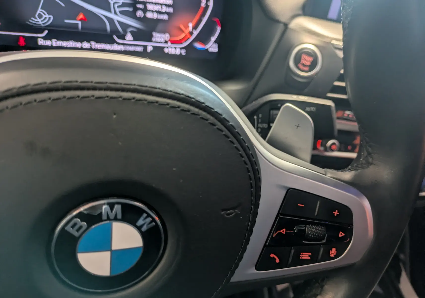 Gros plan sur le volant noir de la BMW X4 blanc, avec commandes intégrées et tableau de bord numérique en arrière-plan.