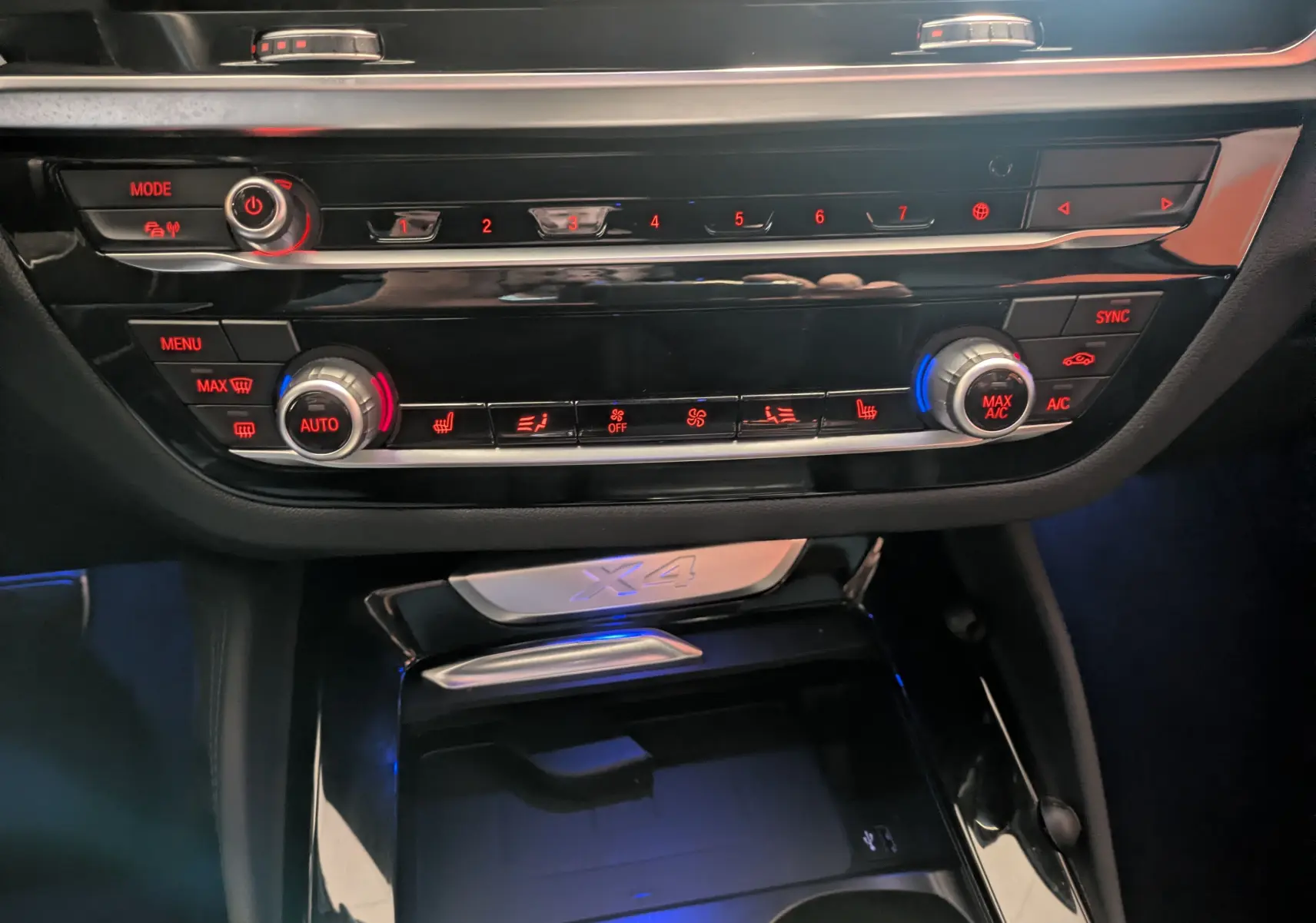 Vue rapprochée de la console centrale du BMW X4 blanc 2021, mettant en valeur les commandes de climatisation et le logo X4 rétroéclairé.