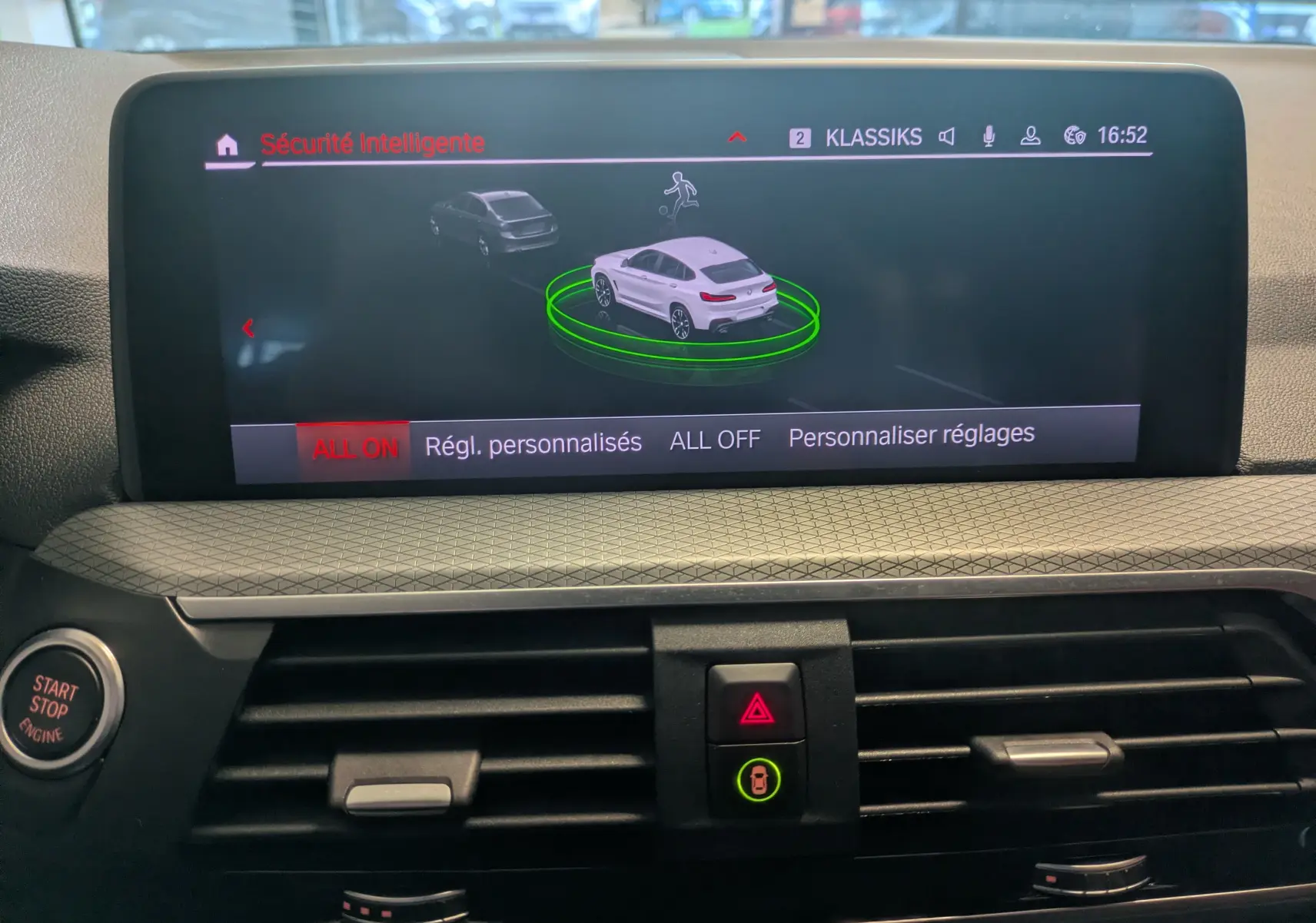 Écran central du BMW X4 blanc 2021 montrant l'interface de sécurité intelligente avec vue 3D du véhicule en surbrillance verte.