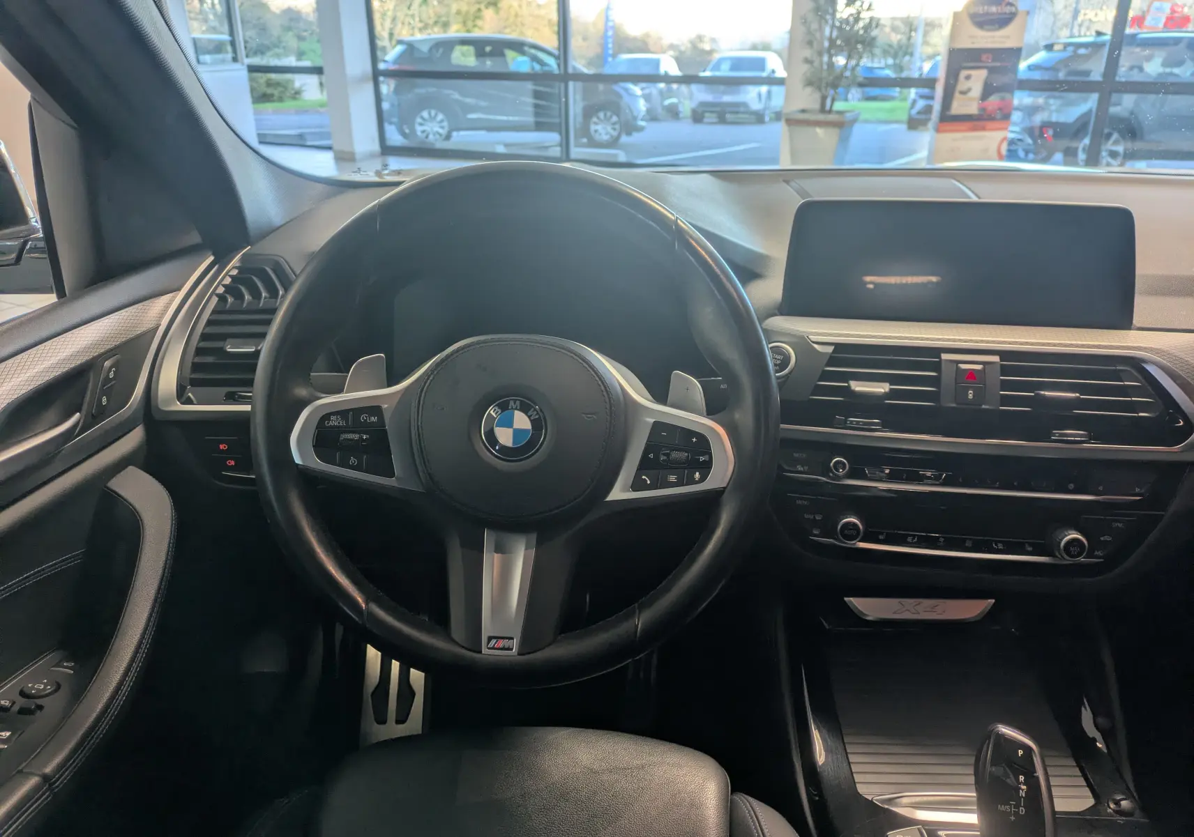 Intérieur de BMW X4 blanc 2021 vu de face, tableau de bord moderne avec volant M Sport et écran central large.