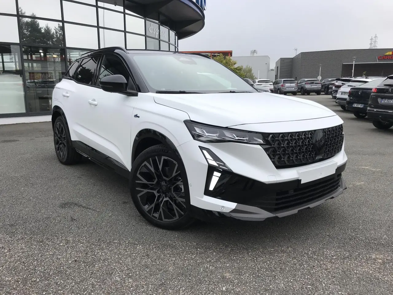 Vue 3/4 avant d'un Renault Austral blanc bi-ton avec calandre noire et jantes alliage noires au design sportif.