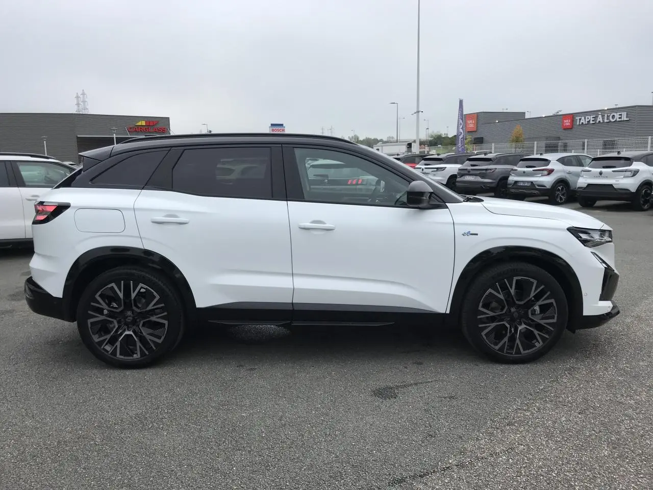 Profil droit du Renault Austral blanc bi-ton avec jantes alliage noires et toit noir satiné, en extérieur sur parking.