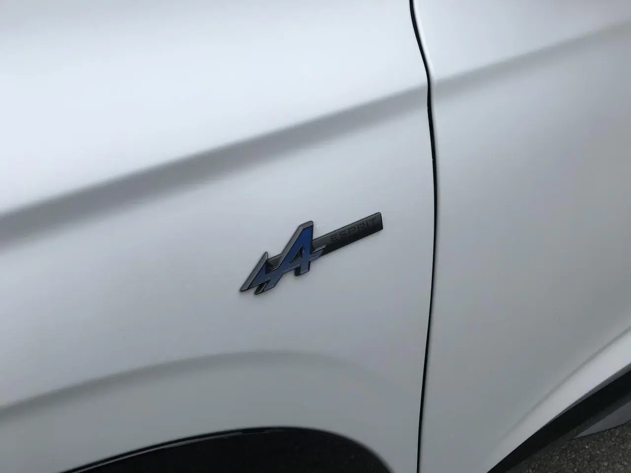 Gros plan sur l'écusson Esprit Alpine bleu sur l'aile avant gauche d'un Renault Austral blanc satin.