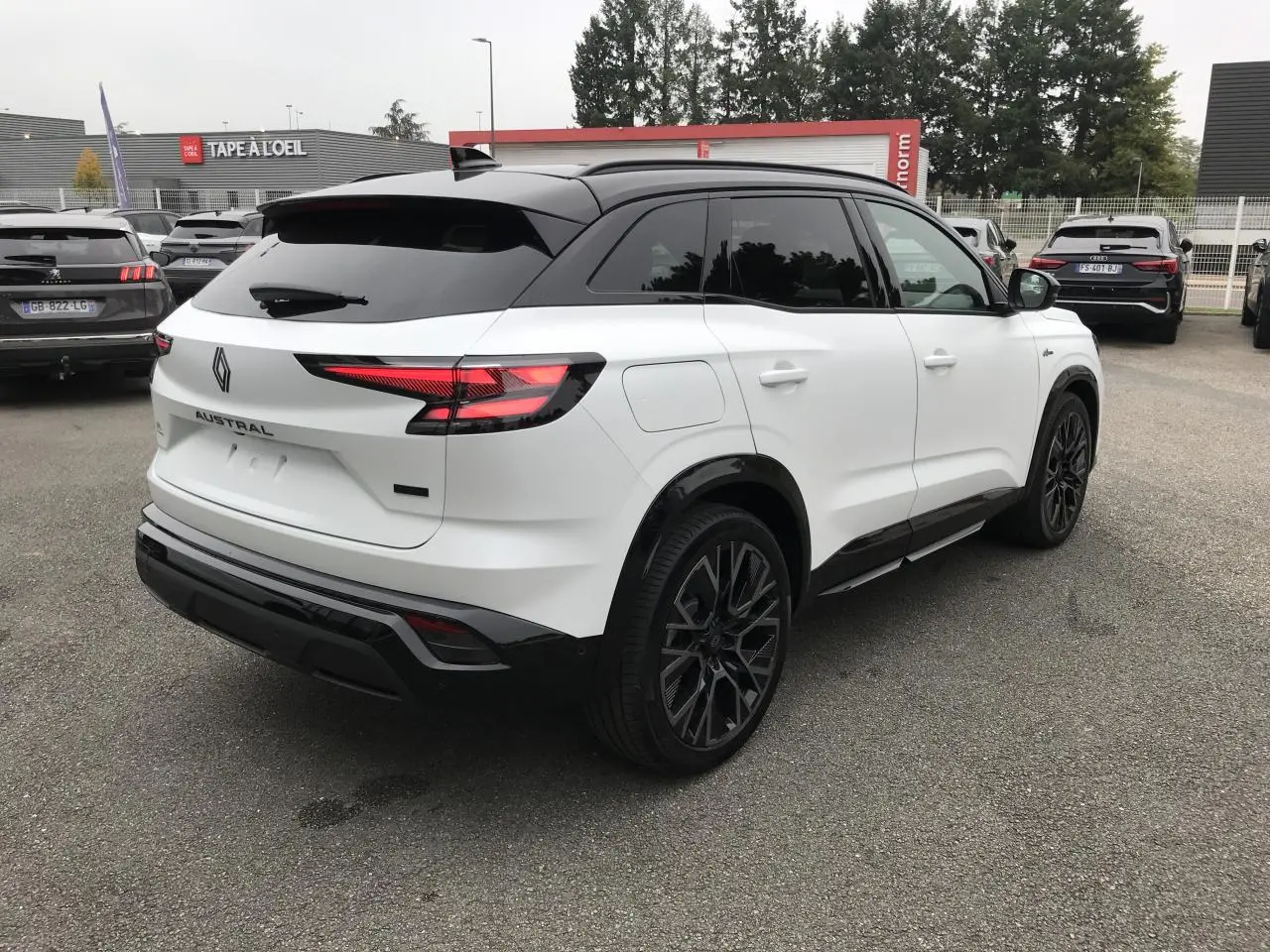 Vue 3/4 arrière droite du Renault Austral blanc bi-ton avec jantes noires et toit noir satin, en extérieur sur parking.