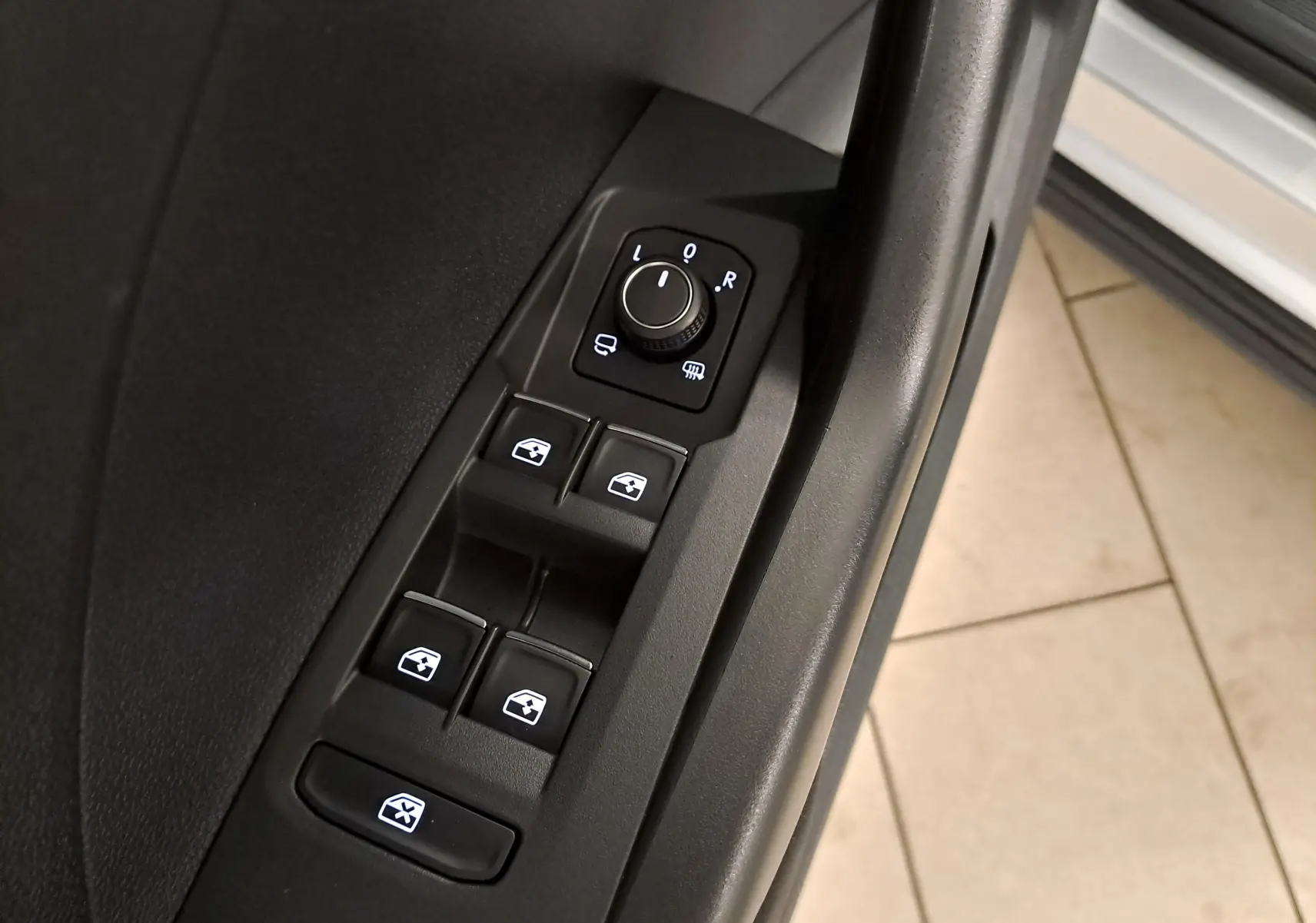 Gros plan sur les commandes de lève-vitres et réglage des rétroviseurs côté conducteur du Volkswagen T-Cross 2022 couleur reflet d'argent.