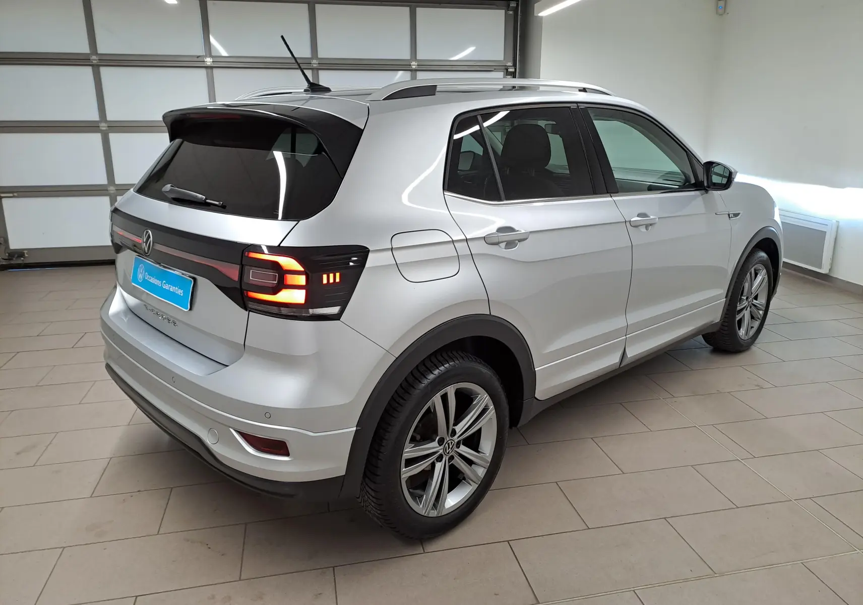 Vue 3/4 arrière droit d'un Volkswagen T-Cross 2022 argent reflet, version R-Line avec feux arrière allumés en intérieur.