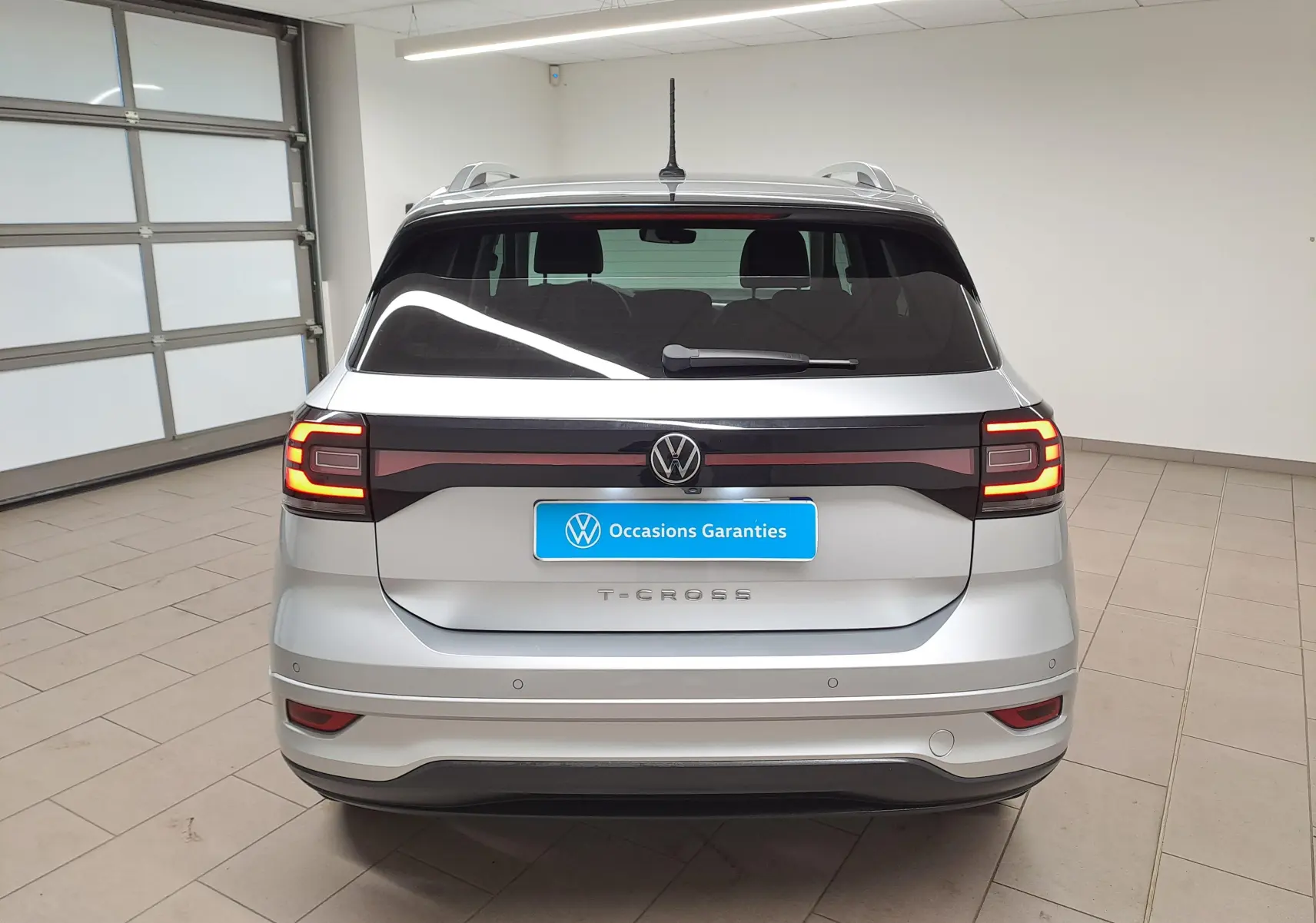 Vue arrière d'un Volkswagen T-Cross 2022 argent reflet avec feux LED allumés et logo VW centré sur le hayon.