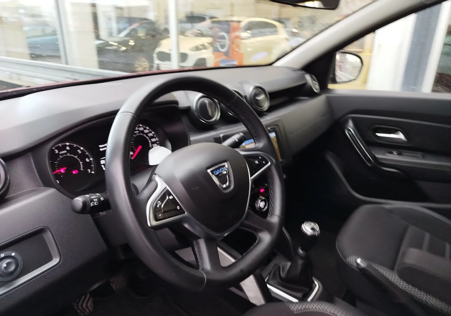 Vue intérieure côté conducteur du Dacia Duster 2020, volant multifonction et levier de vitesses manuel visibles, ambiance noire.