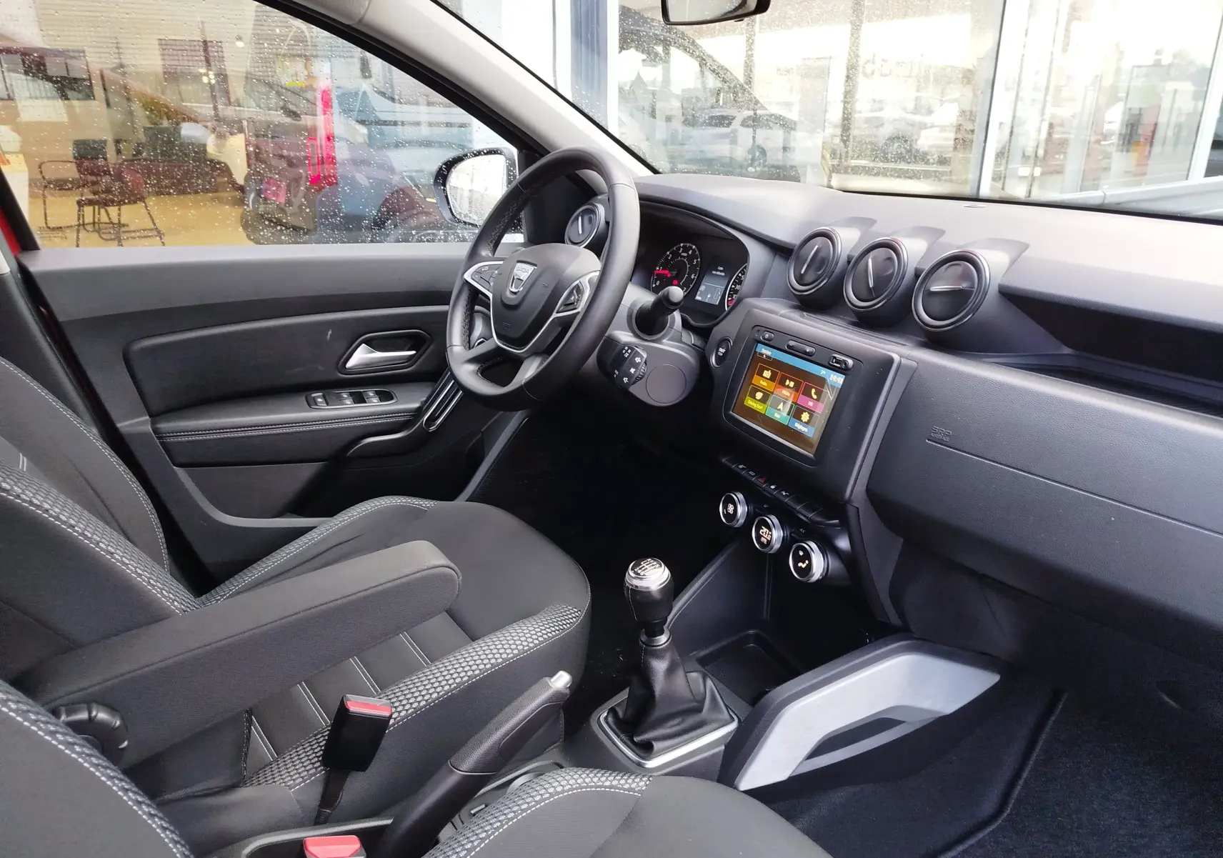 Vue intérieure côté conducteur du Dacia Duster 2020, montrant le volant, la console centrale avec écran tactile et la boîte manuelle.
