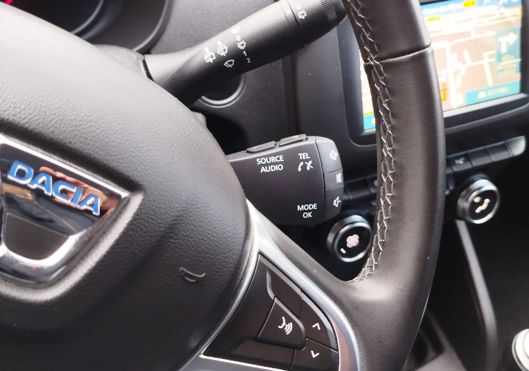 Gros plan sur le volant noir du Dacia Duster rouge Fusion 2020, avec commandes audio et écran tactile en arrière-plan.