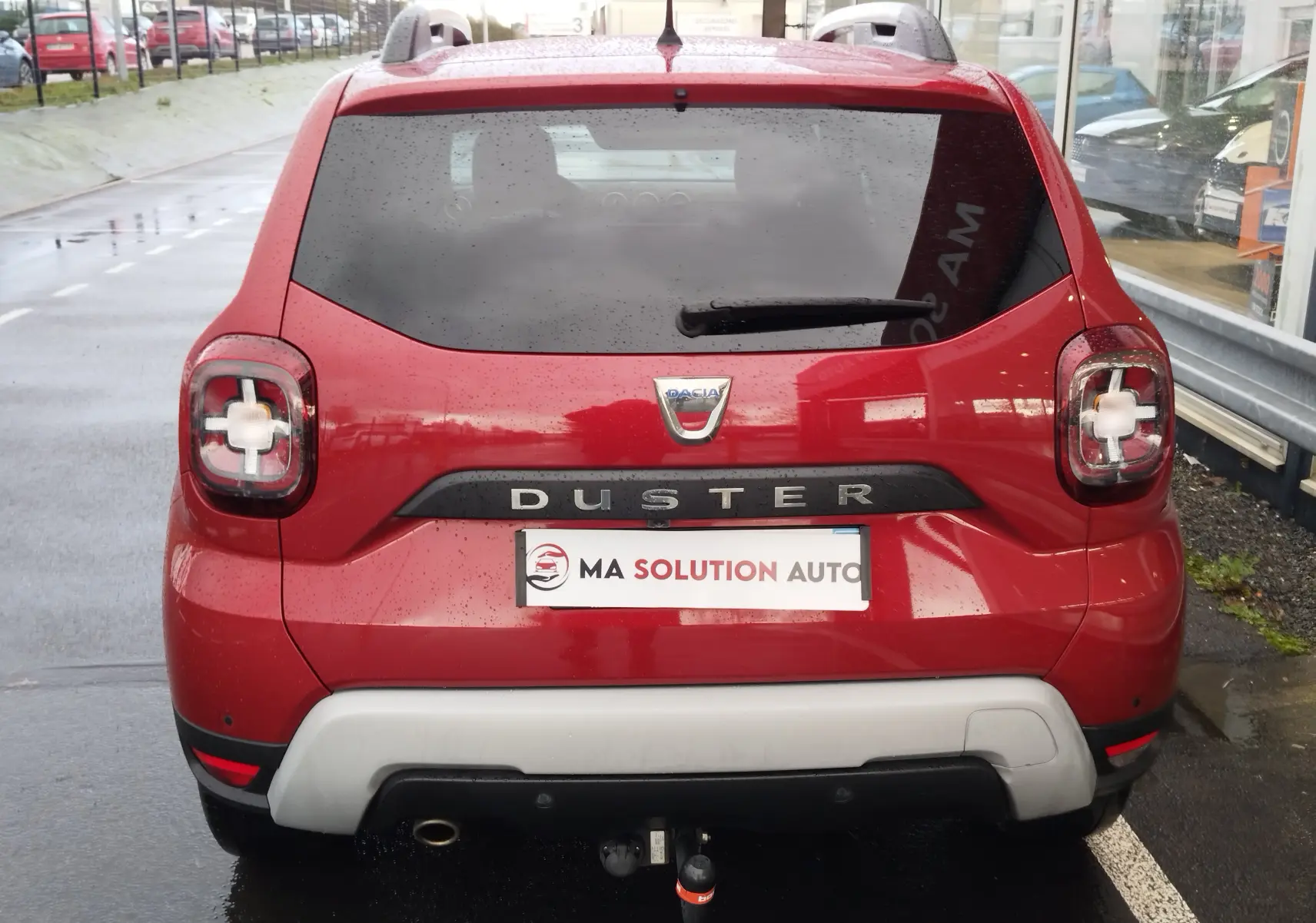 Vue arrière d'un Dacia Duster rouge fusion 2020 avec feux arrière en forme de croix et attelage visible.