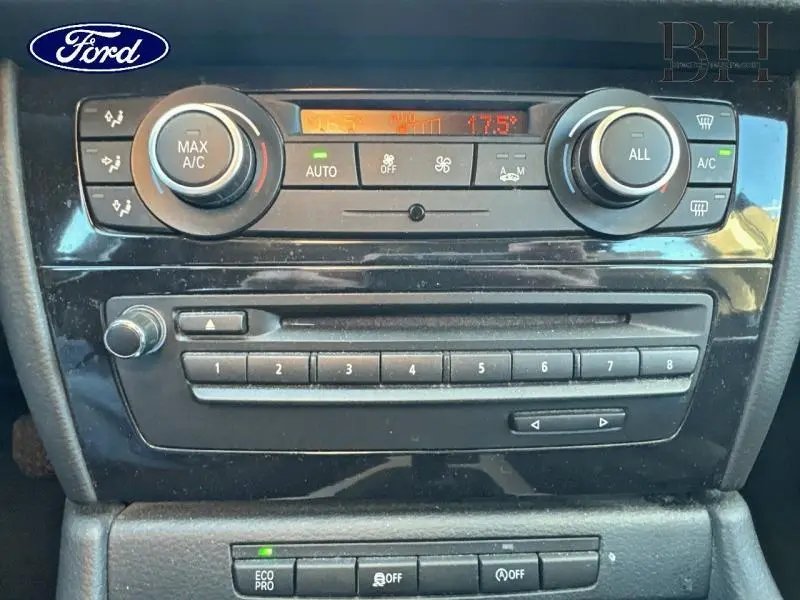 Panneau de commande de climatisation et radio d’une BMW X1 Mineralgrau vue de face, avec commandes circulaires et affichage digital.