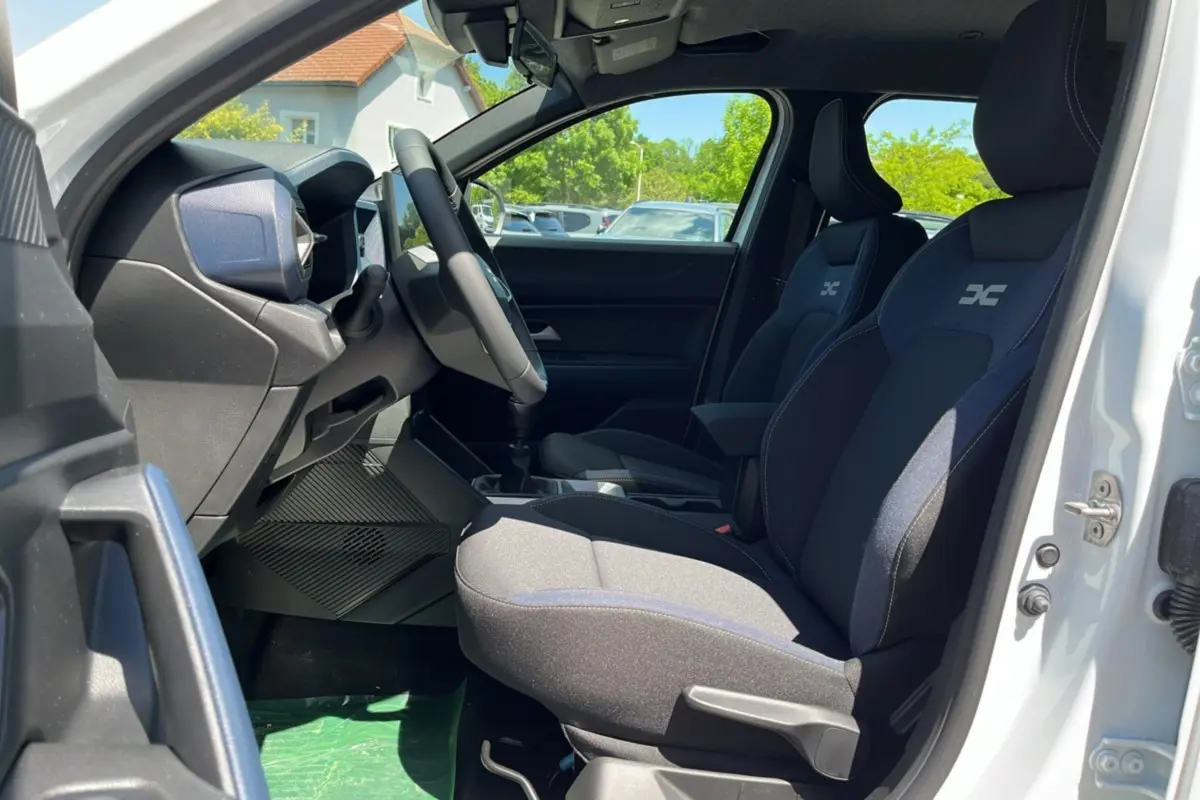 Vue intérieure côté conducteur du Dacia Bigster blanc glacier 2025, sièges tissu avec logo brodé et volant cuir.