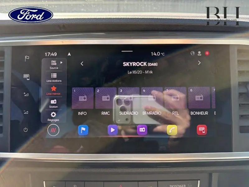 Écran tactile multimédia de la SEAT Ateca 2023 affichant la radio Skyrock, avec reflet de mains et smartphone.