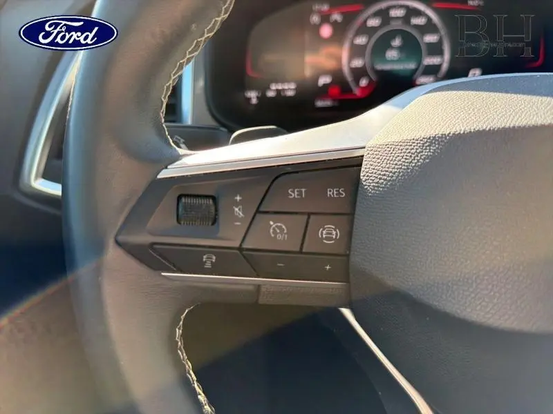 Gros plan sur les commandes au volant cuir noir d'une Ford, avec boutons de régulateur de vitesse et assistance conduite.