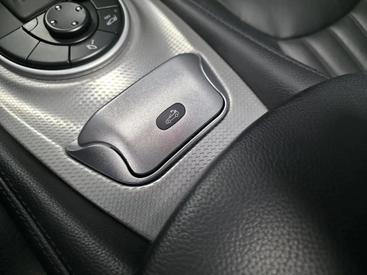 Gros plan sur le bouton d’ouverture du toit rigide dans l’habitacle cuir noir de la Mercedes SL 350 gris.