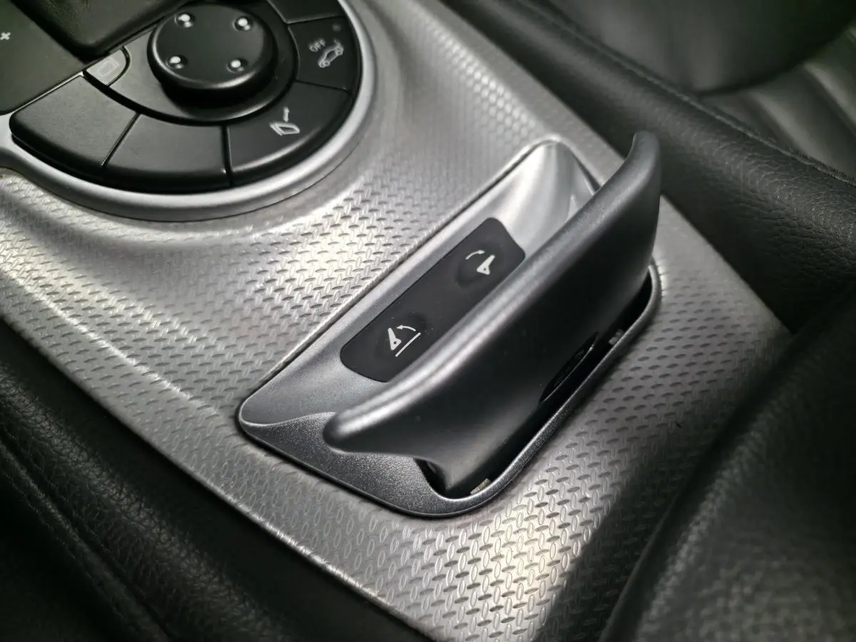 Détail du bouton de commande du toit rigide escamotable sur la console centrale en aluminium brossé d’une Mercedes SL 350 gris.