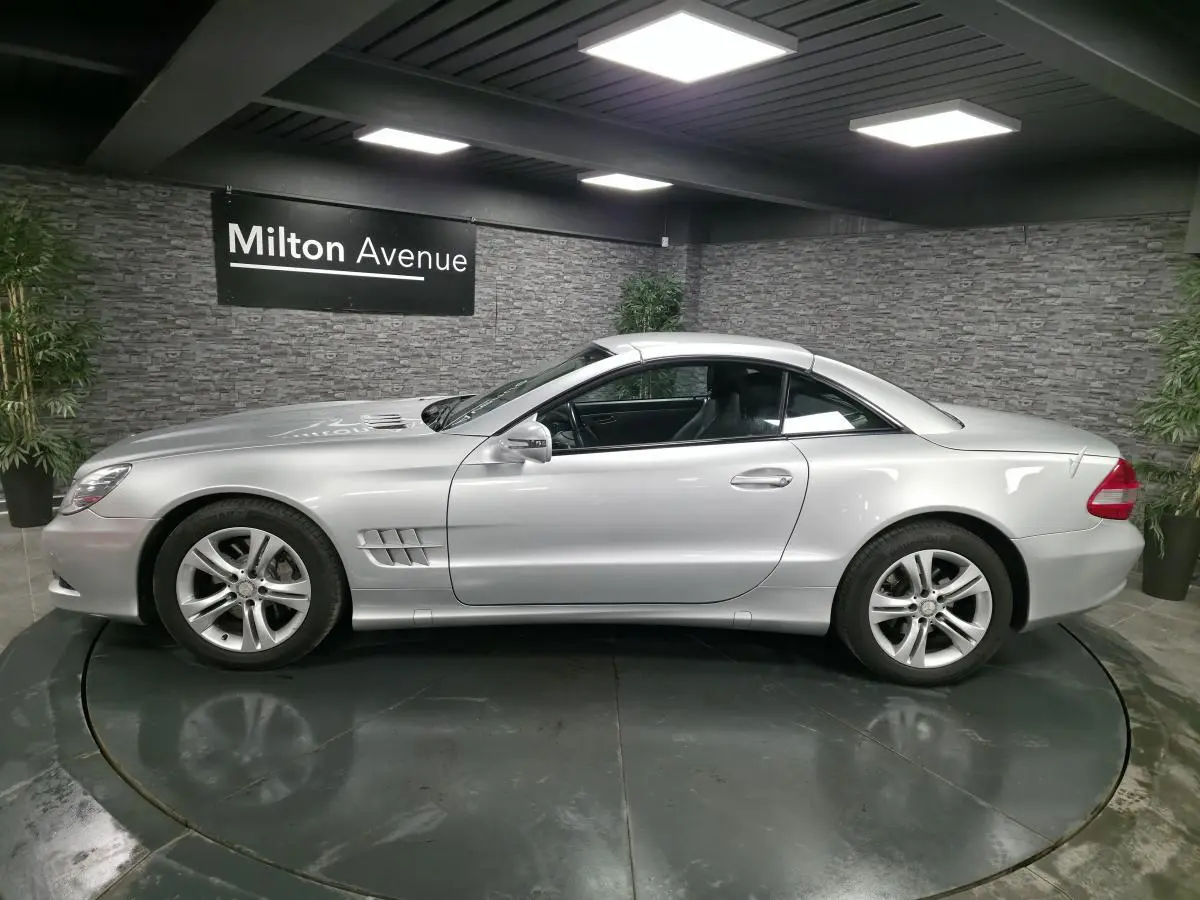 Vue de profil côté gauche d'une Mercedes SL 350 gris métallisé avec toit rigide fermé dans un showroom.
