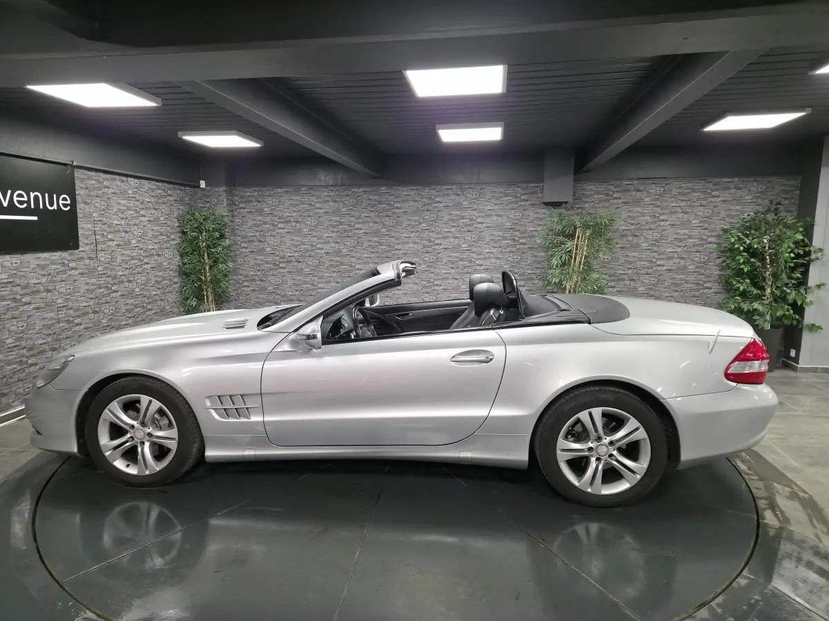 Vue de profil côté gauche d'une Mercedes SL 350 cabriolet gris métallisé avec toit rigide escamotable ouvert.