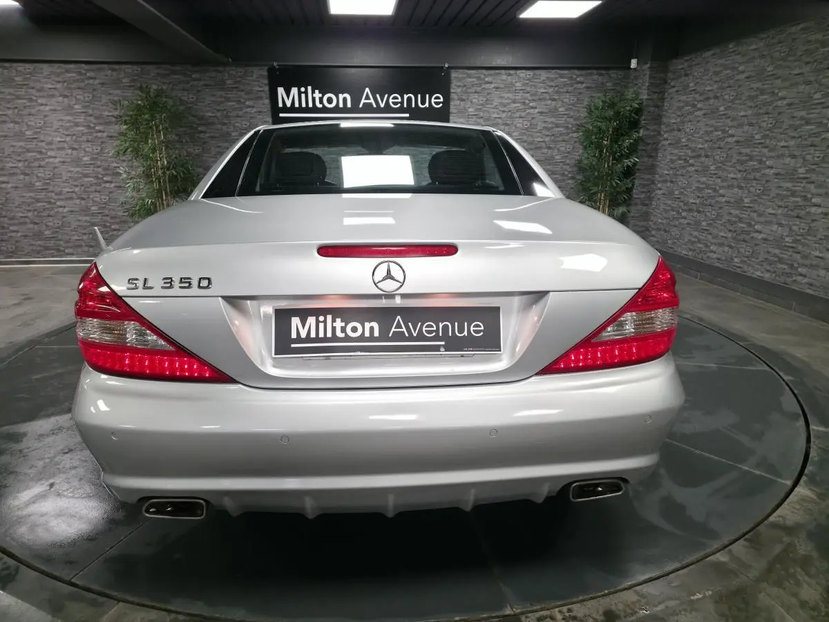 Vue arrière d'une Mercedes SL 350 gris clair, avec feux rouges allumés et double sortie d'échappement chromée.
