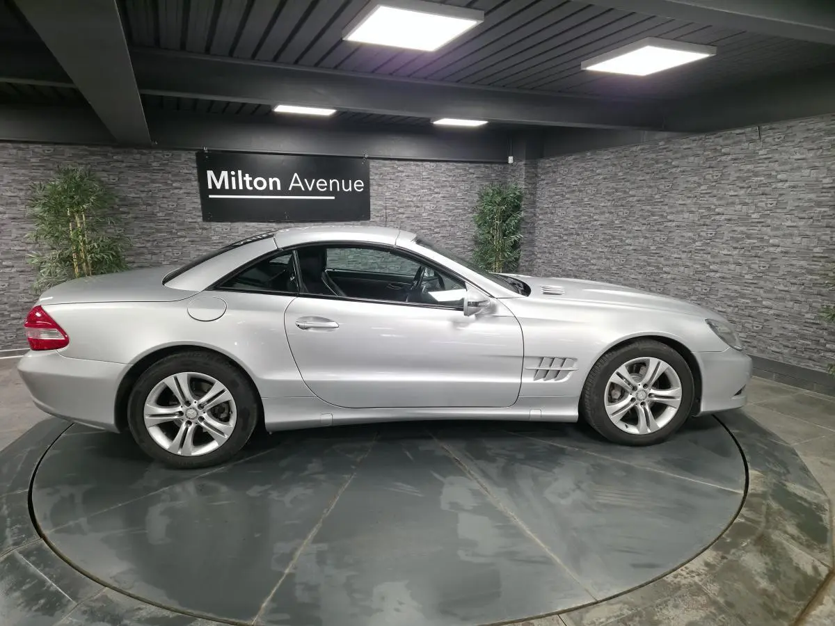 Vue de profil côté gauche d'une Mercedes SL 350 gris métallisé avec toit rigide fermé dans un showroom.