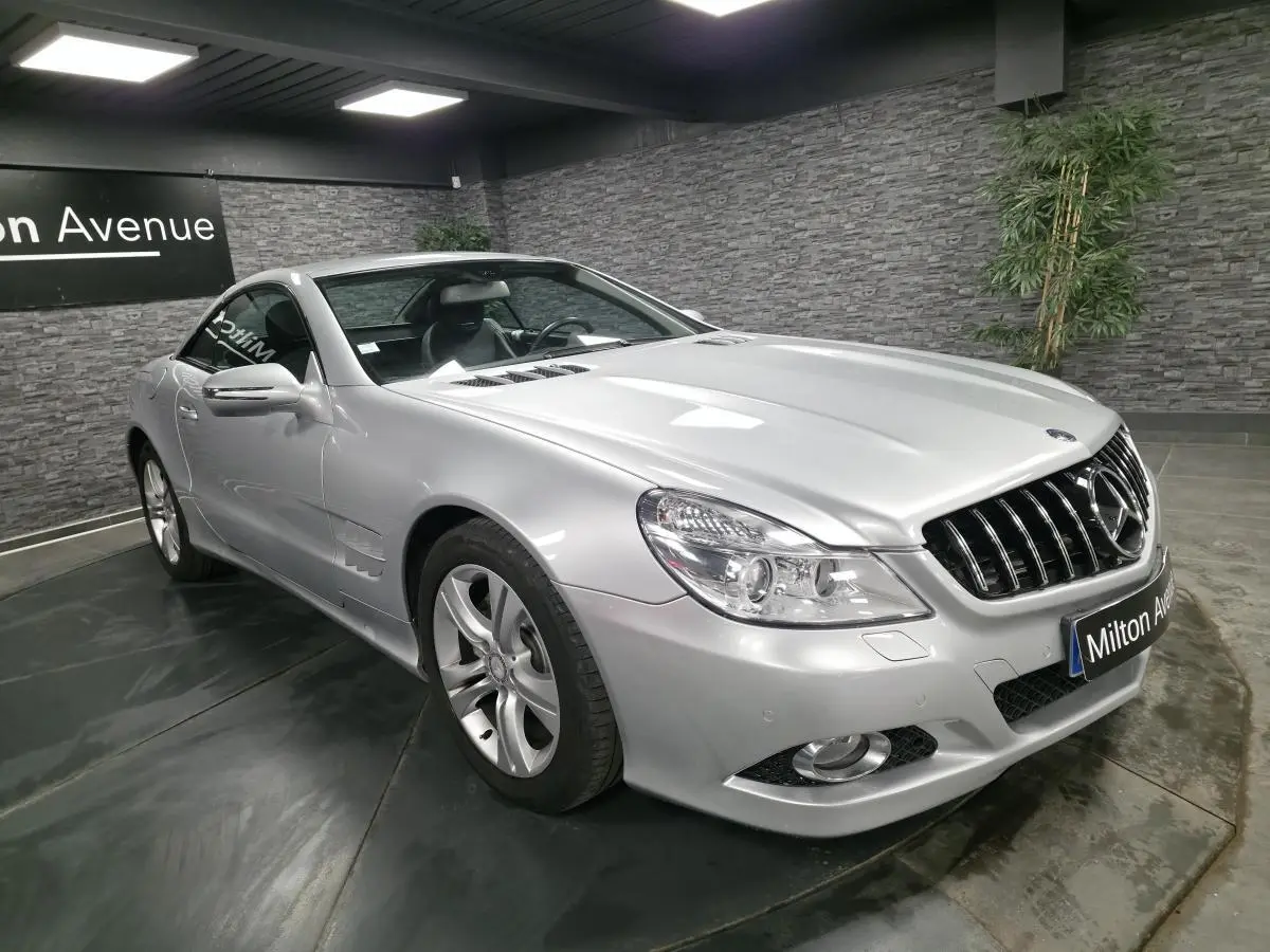 Vue 3/4 avant droite d'une Mercedes SL 350 gris métallisé avec jantes alliage et calandre chromée dans un showroom.