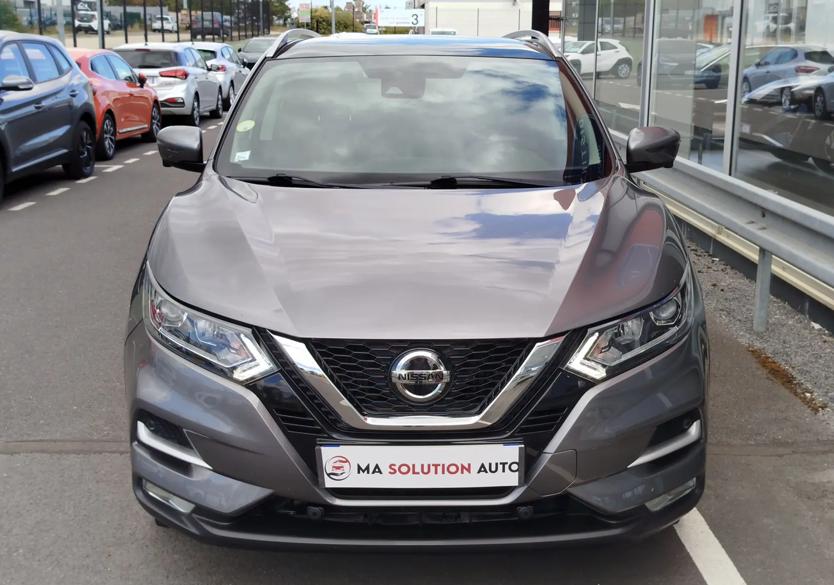 Vue frontale d'un Nissan Qashqai gris Squale 2021 avec calandre chromée et phares LED allumés.
