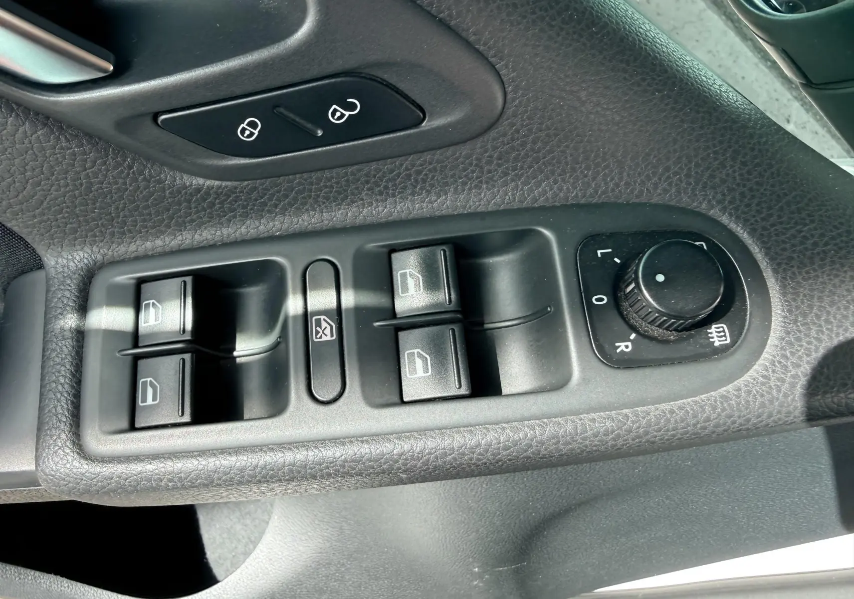 Gros plan sur les commandes de lève-vitres et réglage des rétroviseurs côté conducteur d'une Volkswagen Golf blanche de 2012.