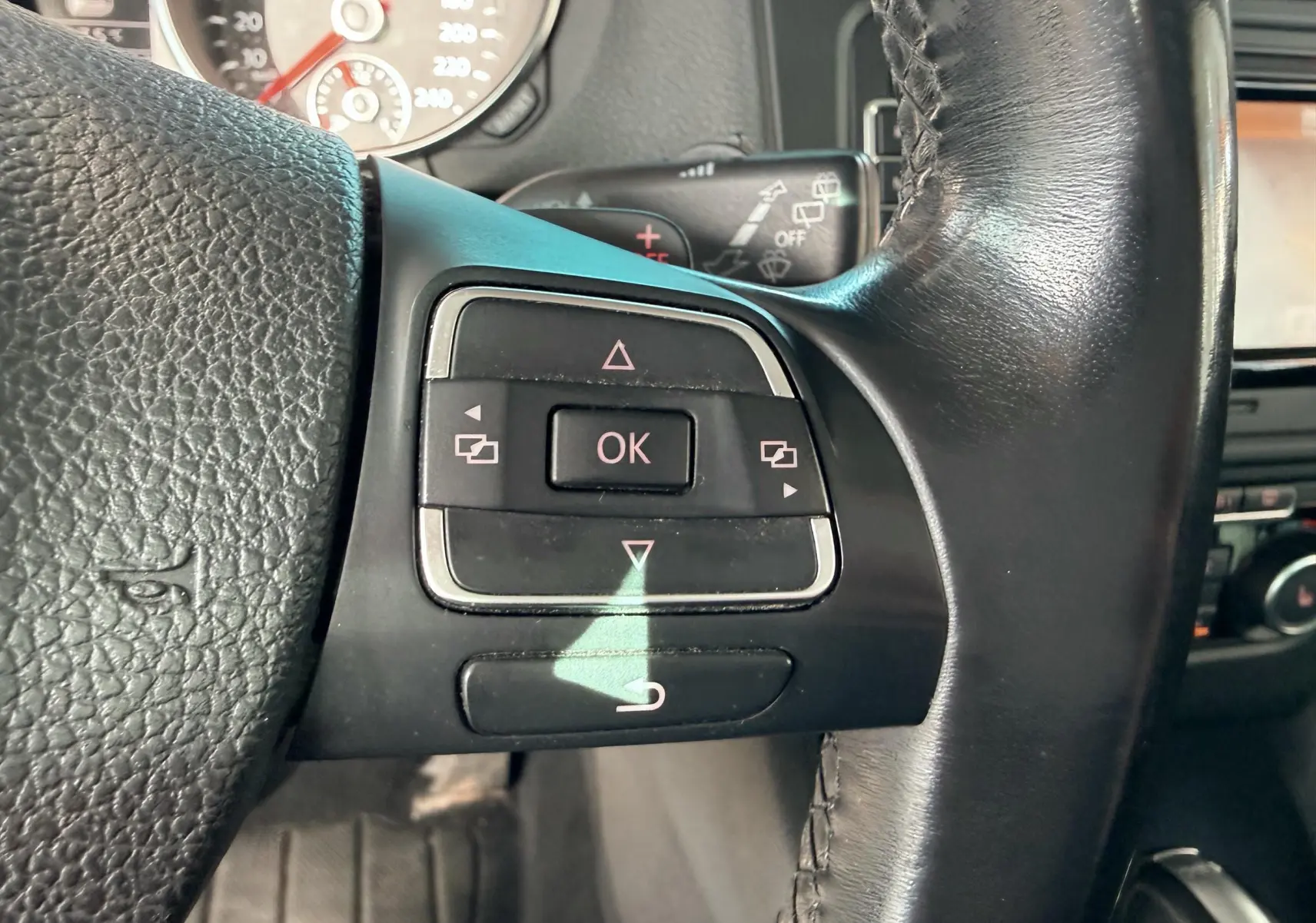 Gros plan sur les commandes multifonctions du volant en cuir noir d'une Volkswagen Golf blanche de 2012.