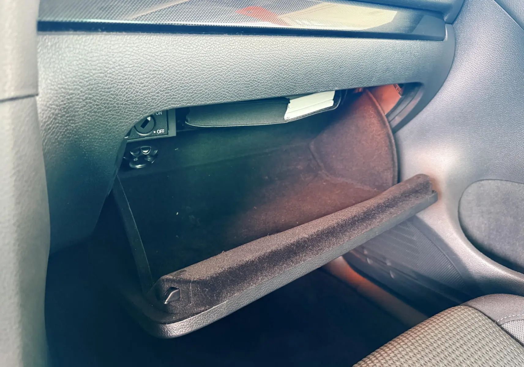 Gros plan sur la boîte à gants ouverte côté passager d'une Volkswagen Golf blanche, intérieur gris noir.