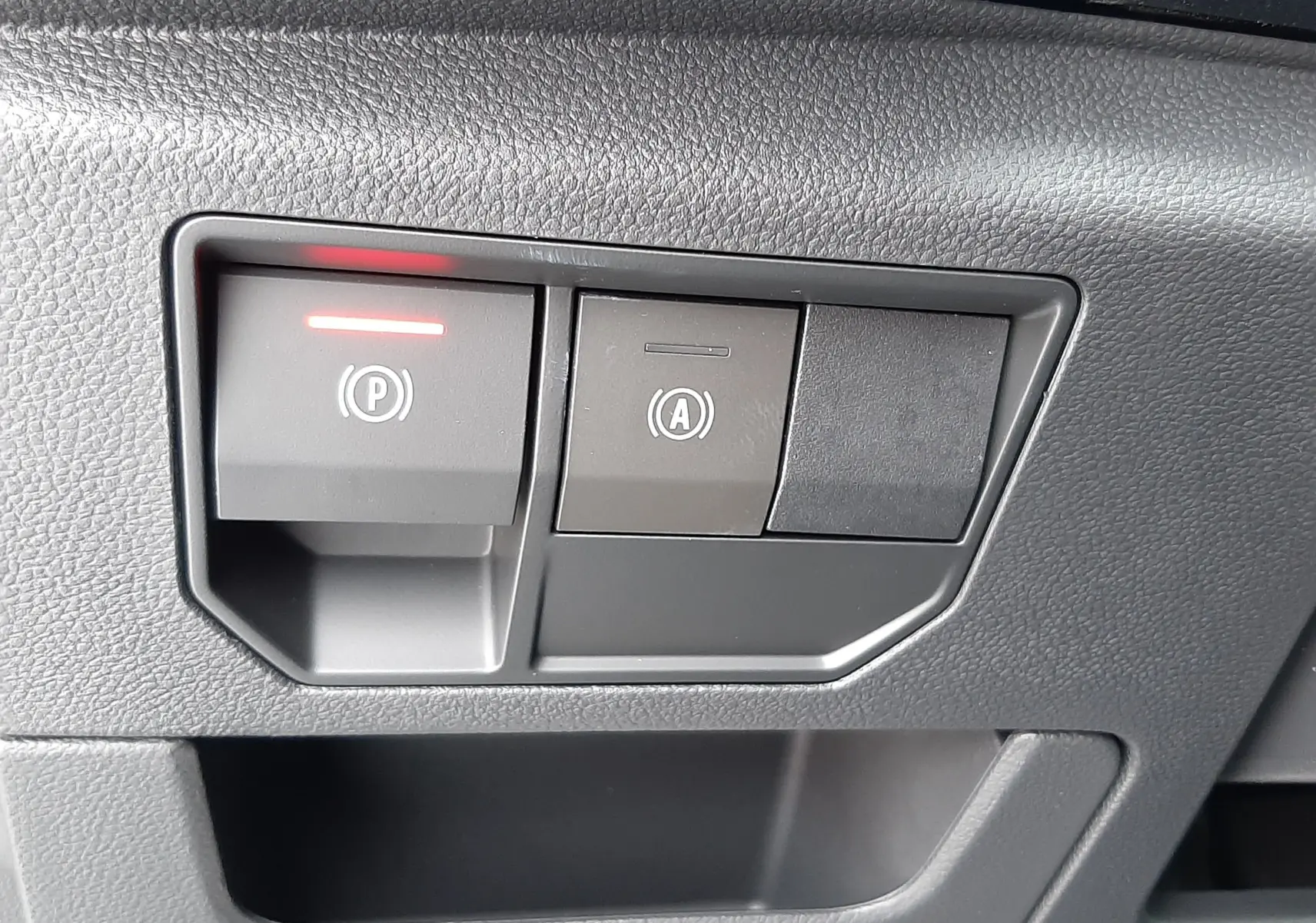 Gros plan sur les boutons de commande du frein à main électrique et de l'arrêt automatique du moteur dans un Renault Austral gris schiste.