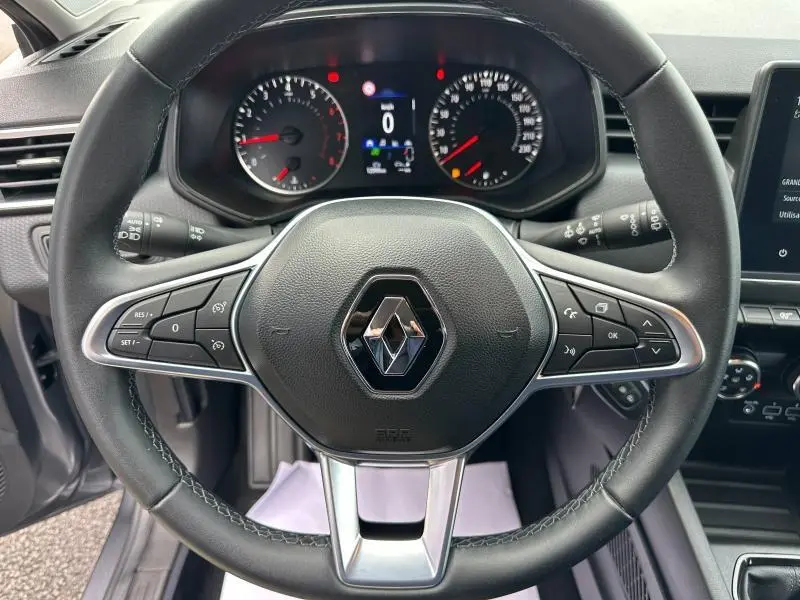 Vue centrée sur le volant de la Renault Clio 2023 gris schiste, avec commandes intégrées et tableau de bord numérique.