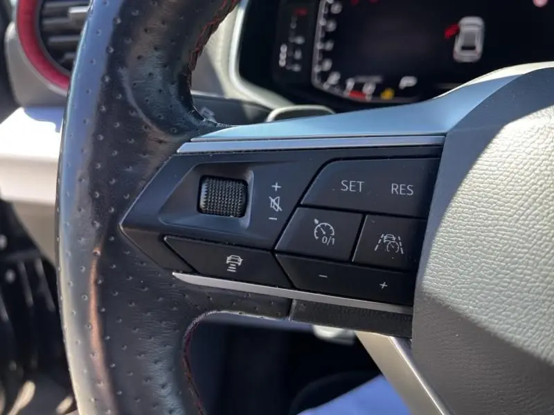 Gros plan sur les commandes du volant en cuir perforé noir de la SEAT Ibiza 2022, avec boutons de régulateur et assistance.