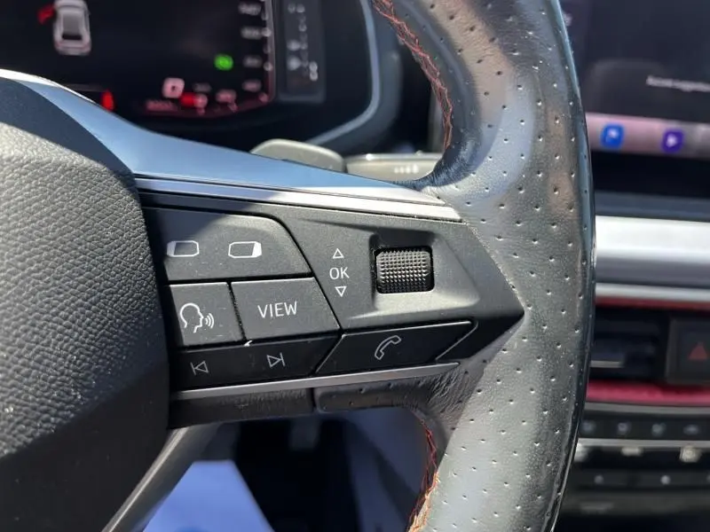 Gros plan sur les commandes du volant perforé avec surpiqûres rouges de la SEAT Ibiza bleu foncé 2022, version FR Xclusive.