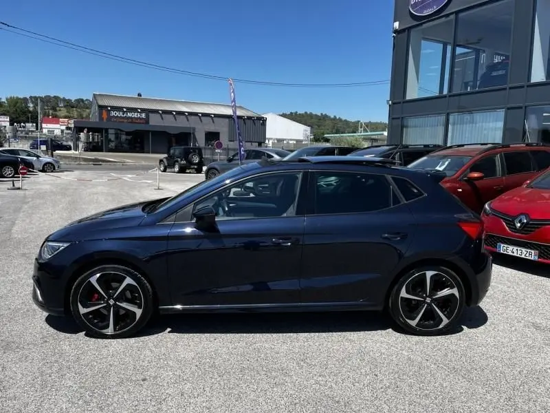 Vue de profil côté gauche d'une SEAT Ibiza 2022 bleu foncé métal avec jantes noires et rouges, garée en extérieur.